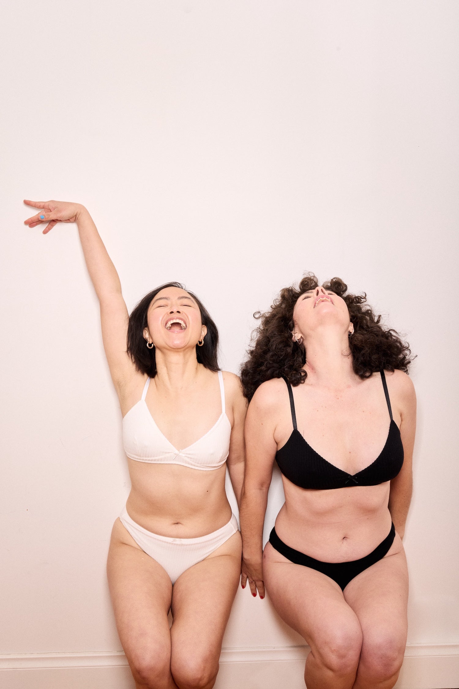 Two women wearing black and white underwear sets against a plain background