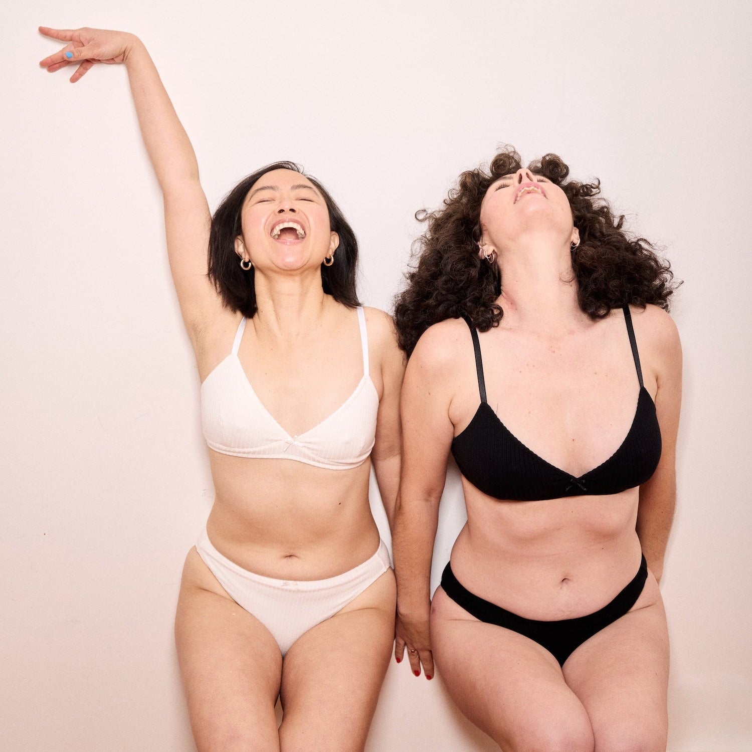 Two women wearing black and white underwear sets against a plain background